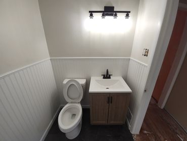 Small bathroom with toilet and wooden vanity under bright light fixture.