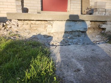 Damaged concrete step with visible cracks and rubble beneath a red door.