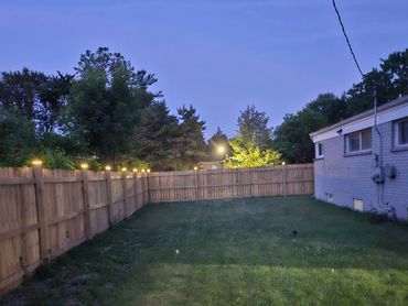 A backyard with a wooden fence and evening lighting.