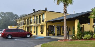 Exterior view of a yellow two-story motel with parked cars and palm trees.