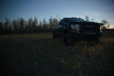 Black GMC pickup truck parked in a field at dusk.