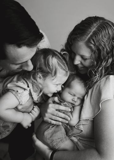 A tender family moment with parents and their two young children in black and white.