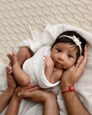 Newborn baby wrapped in white, gently held by loving hands.