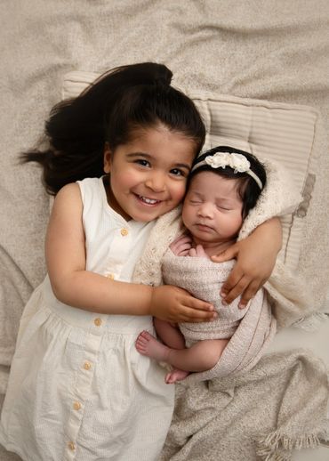 A happy young girl lovingly embraces her sleeping newborn sibling wrapped in a soft blanket.
