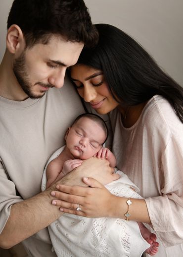 Tender moment of new parents cradling their sleeping newborn wrapped in a white blanket.