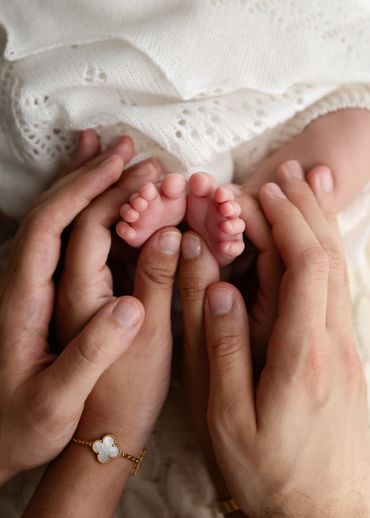 Adults gently holding a newborn's tiny feet wrapped in a white blanket.