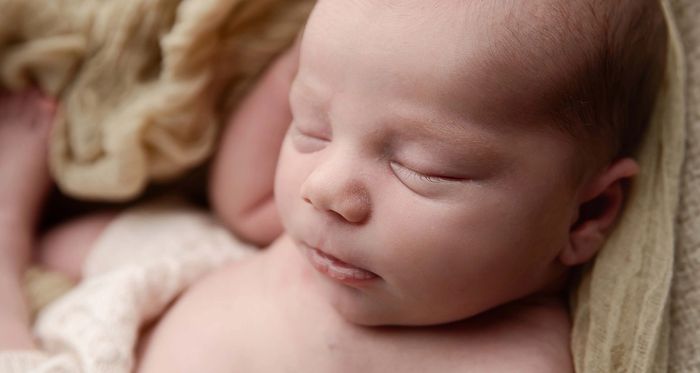 Close-up of a peacefully sleeping newborn baby wrapped in soft beige fabric.