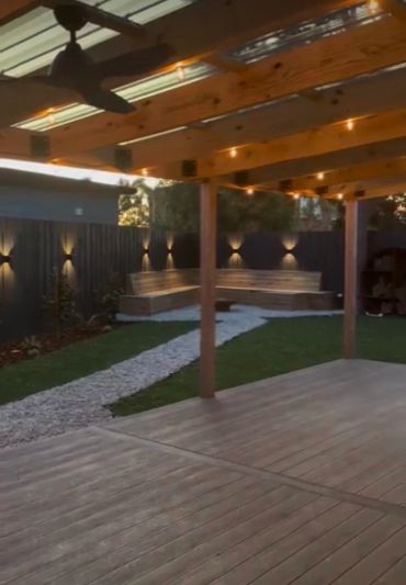 Cozy backyard with wooden deck, overhead fan, and ambient lighting along a dark fence.