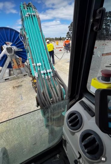 View from inside construction machinery showing hydraulic hoses and workers outside.