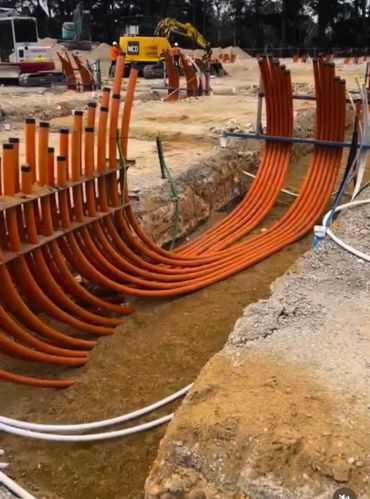 Neatly organized orange conduit pipes at a construction site trench.