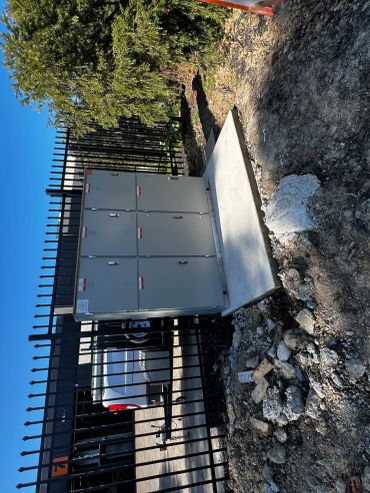 Outdoor electrical control panel mounted on a concrete slab near a fence.