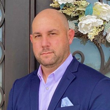 Man in blue suit with flowers behind him.