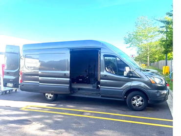 Gray cargo van with open sliding and rear doors parked outside on a sunny day.