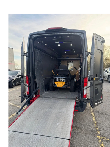 Rear view of a van with open doors and a ramp, carrying a lawn mower inside.
