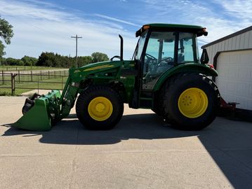 Green tractor parked next to a building under a blue sky.
