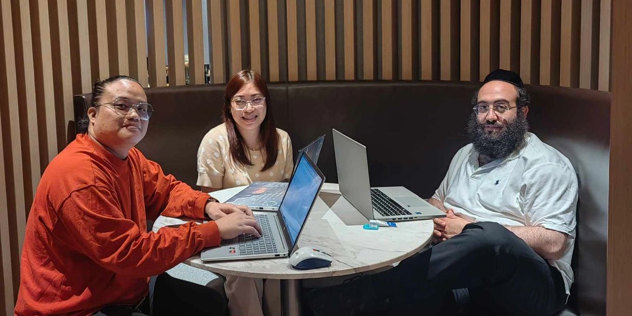 Three people with laptops sitting around a round table in a cozy workspace.