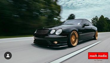 Black luxury car with gold rims driving fast on a road.