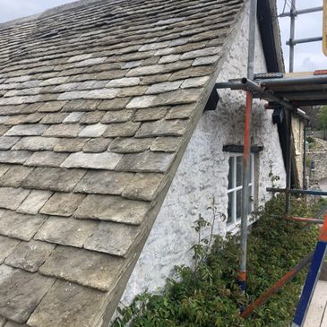 Old stone slate roof on a white cottage with scaffolding.