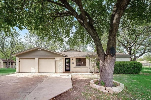 a tan brick home with a tree in front yard