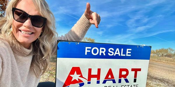 Linsey Ahart Taylor pointing to Ahart Real Estate for sale sign.