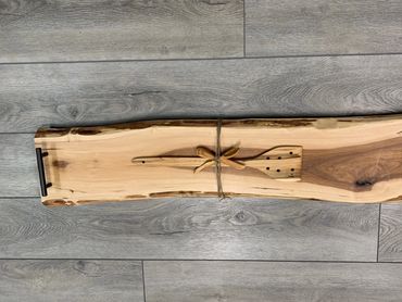 Handcrafted wooden serving board with utensils tied on top.