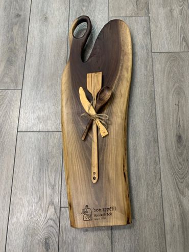 Wooden cutting board with utensils and personalized engraving.