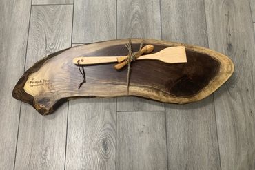 Rustic wooden serving board engraved with names and date, tied with wooden utensils.