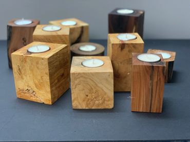 Wooden cube candle holders with white tea candles on a dark surface.