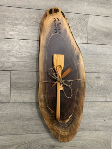 Rustic wooden cutting board with two wooden utensils tied together on top.