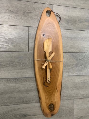 Rustic wooden cutting board with tied wooden utensils on a gray floor.
