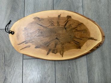 Oval wooden cutting board with unique central pattern and leather strap.