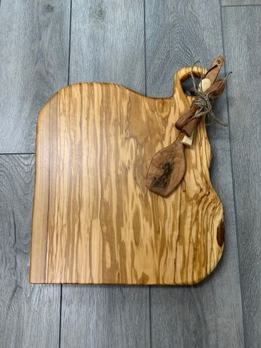 Wooden cutting board with small tied wooden utensils on a gray floor.