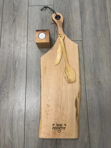 Wooden cutting board with utensils and a candle holder on gray floor.