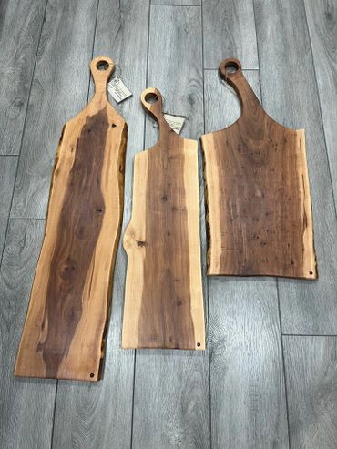 Three handcrafted wooden cutting boards with natural edges on a gray floor.