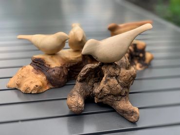 Wooden bird sculptures perched on rustic wood pieces on a gray table.