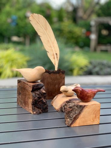 Wooden bird sculptures displayed on natural wood blocks outdoors.