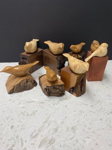 Wooden bird sculptures displayed on natural wood bases.