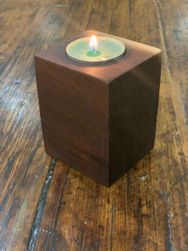 A lit tealight candle in a wooden cube holder on a wooden surface.