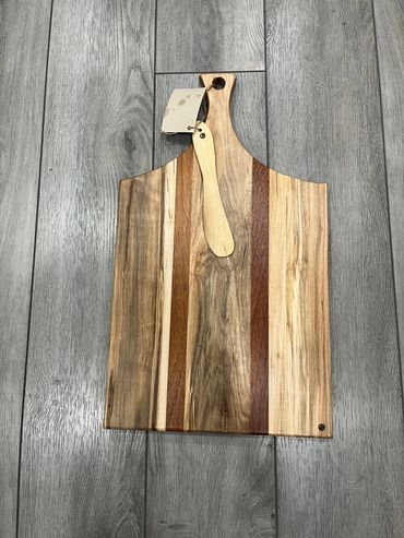 Wooden cutting board with a small wooden spreader on a gray wooden floor.