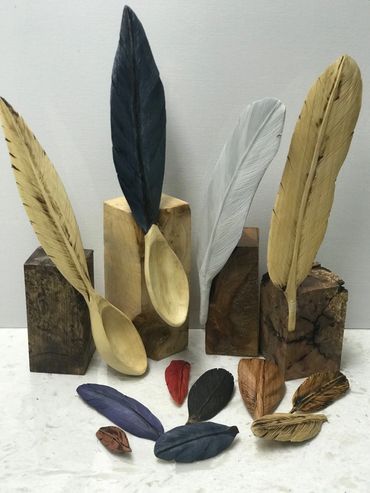 Hand-carved wooden spoons and decorative feathers displayed on wooden blocks.