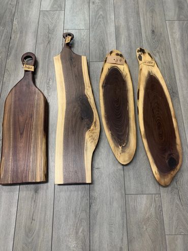 Four unique wooden cutting boards with price tags on a wooden floor.
