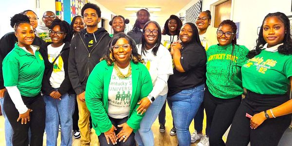 Group of diverse students smiling indoors, some wearing Kentucky State University apparel.
