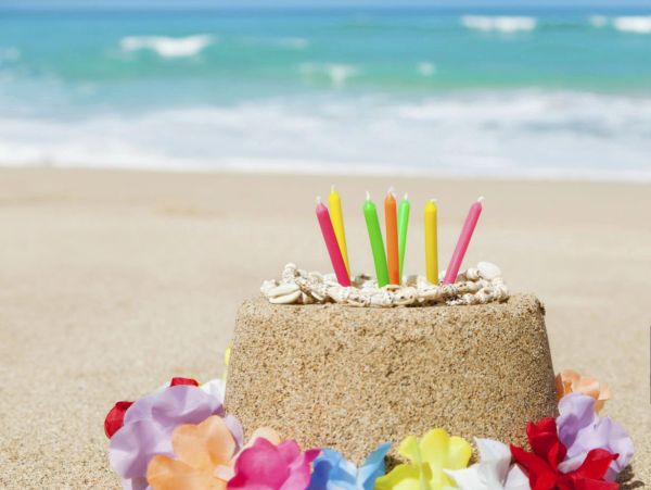 A colorful sand cake with candles on a beach shore.