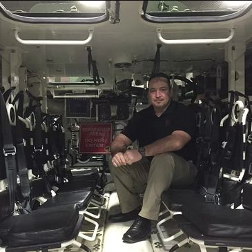 Man sitting inside a military vehicle with secured seats and a restricted area sign.