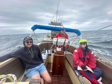 Three people relaxing on a sailboat in cloudy weather.