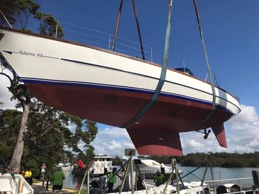 A sailboat named Adams 45 is being lifted out of the water.