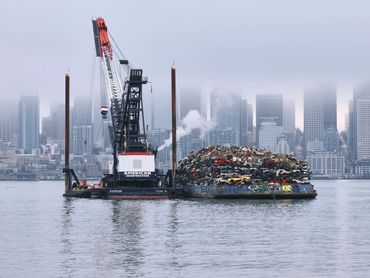 Industrial construction photo of scrap barge and floating crane with Seattle foggy skyline backgroun