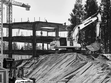 Construction site photo of steel building and excavator in action.