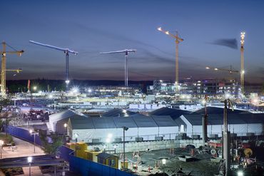 Construction photo of multiple cranes lit up at twilight.