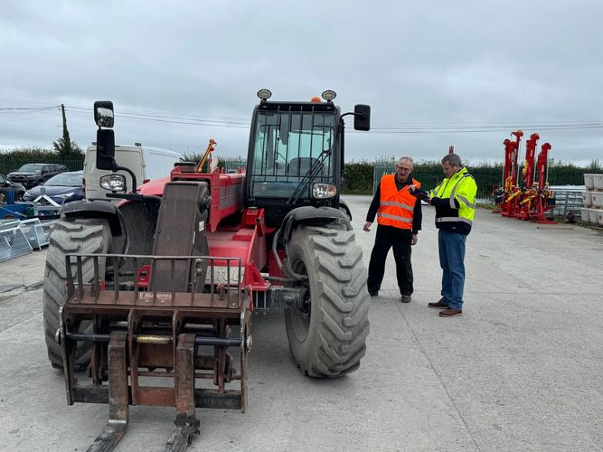 Two men in safety vests inspecting a large red forklift in an industrial yard.